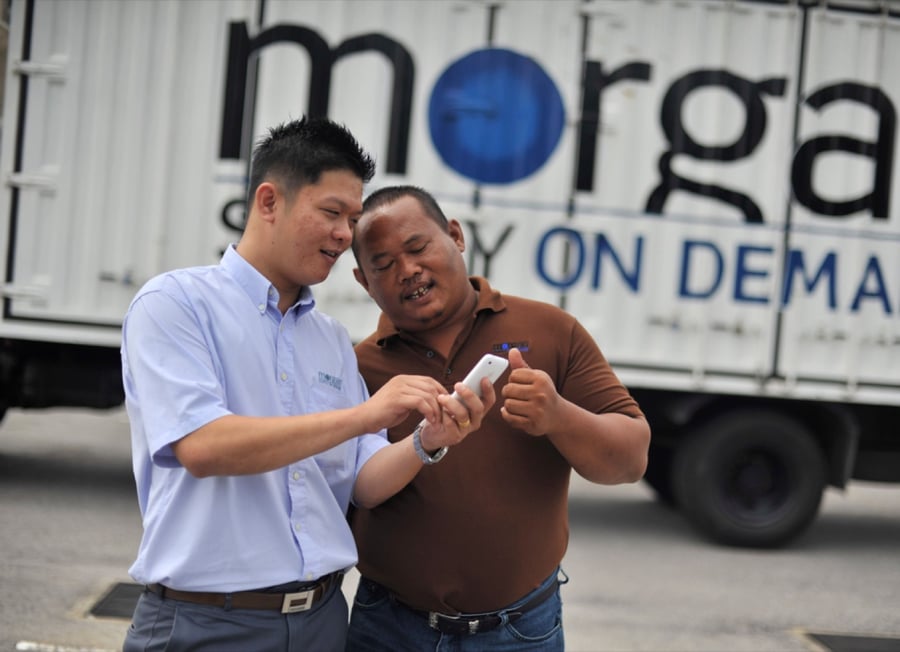 Morgan team members reviewing a shipment update on a phone beside a Morgan truck